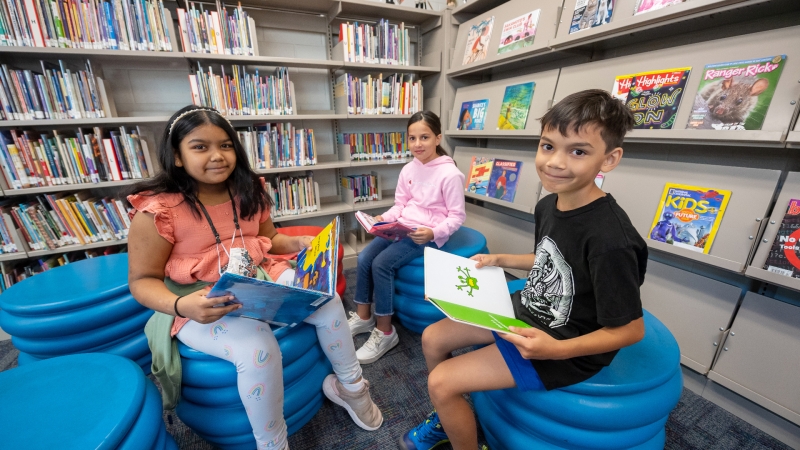 two students sitting on chairs in a school library reading books