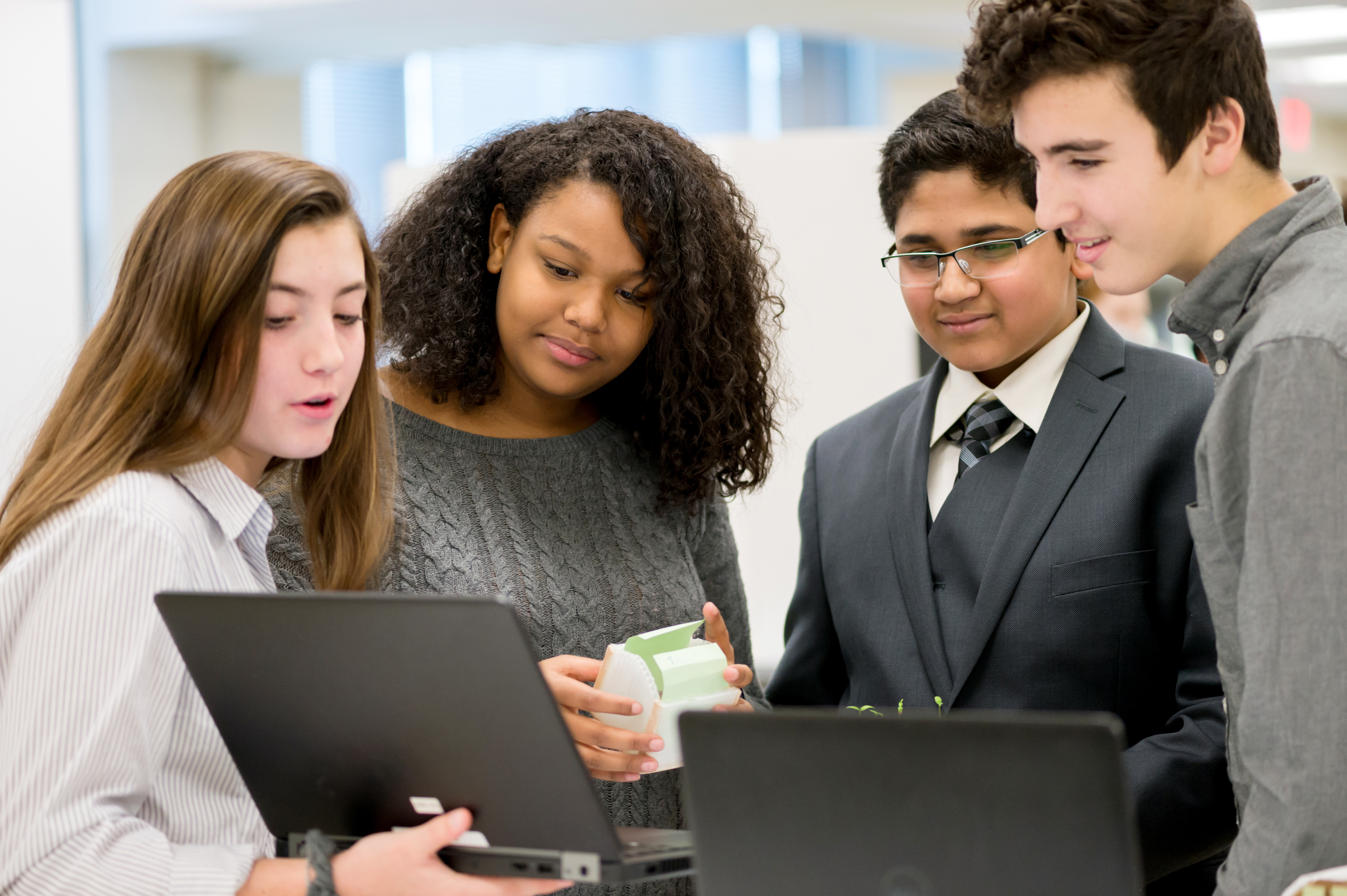 four high school aged students collaborating on a project on a laptop