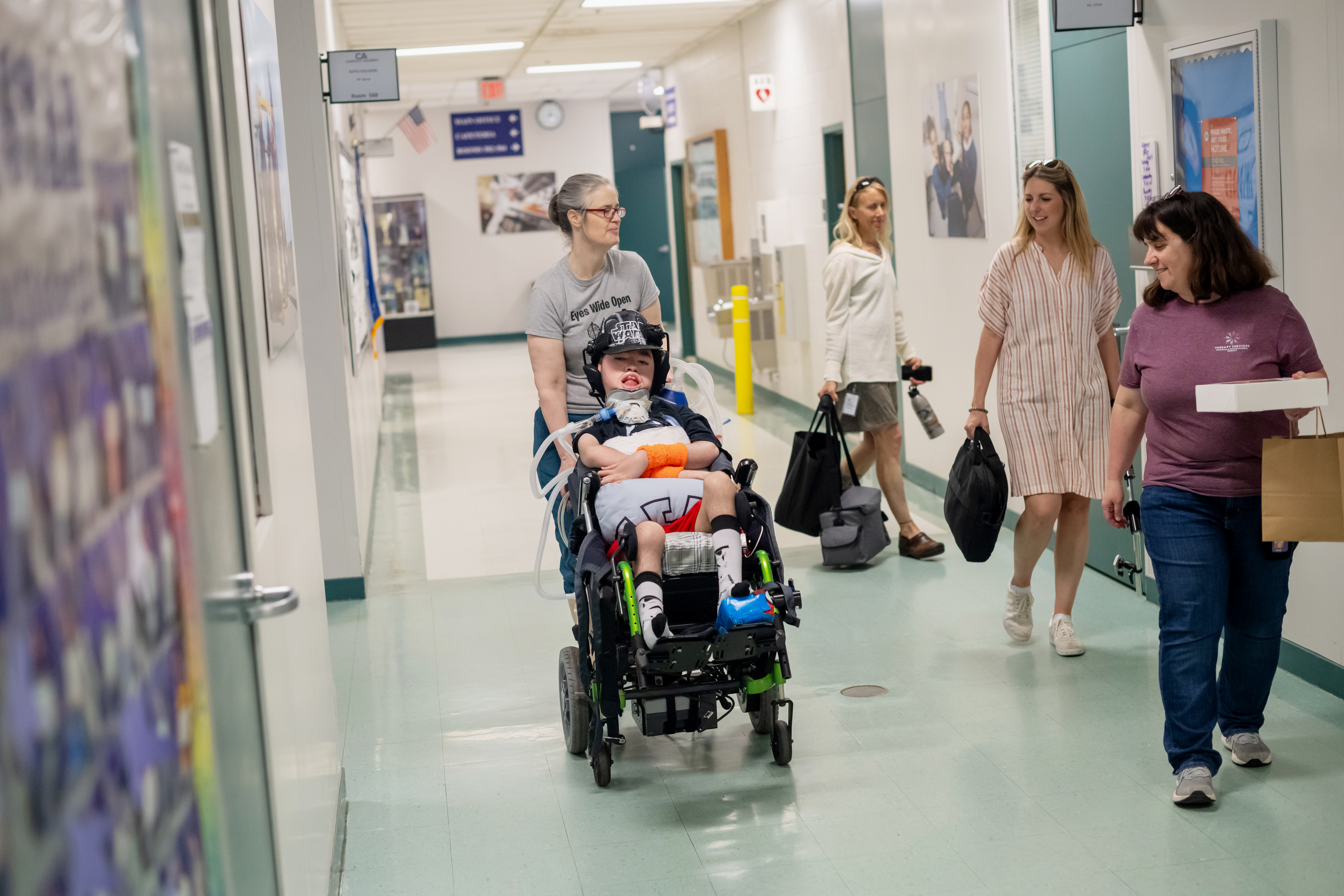 Jamie Bruen pushes his son, Liam, into Chantilly Academy. Three FCPS staff members smile and walk alongside his wheelchair.