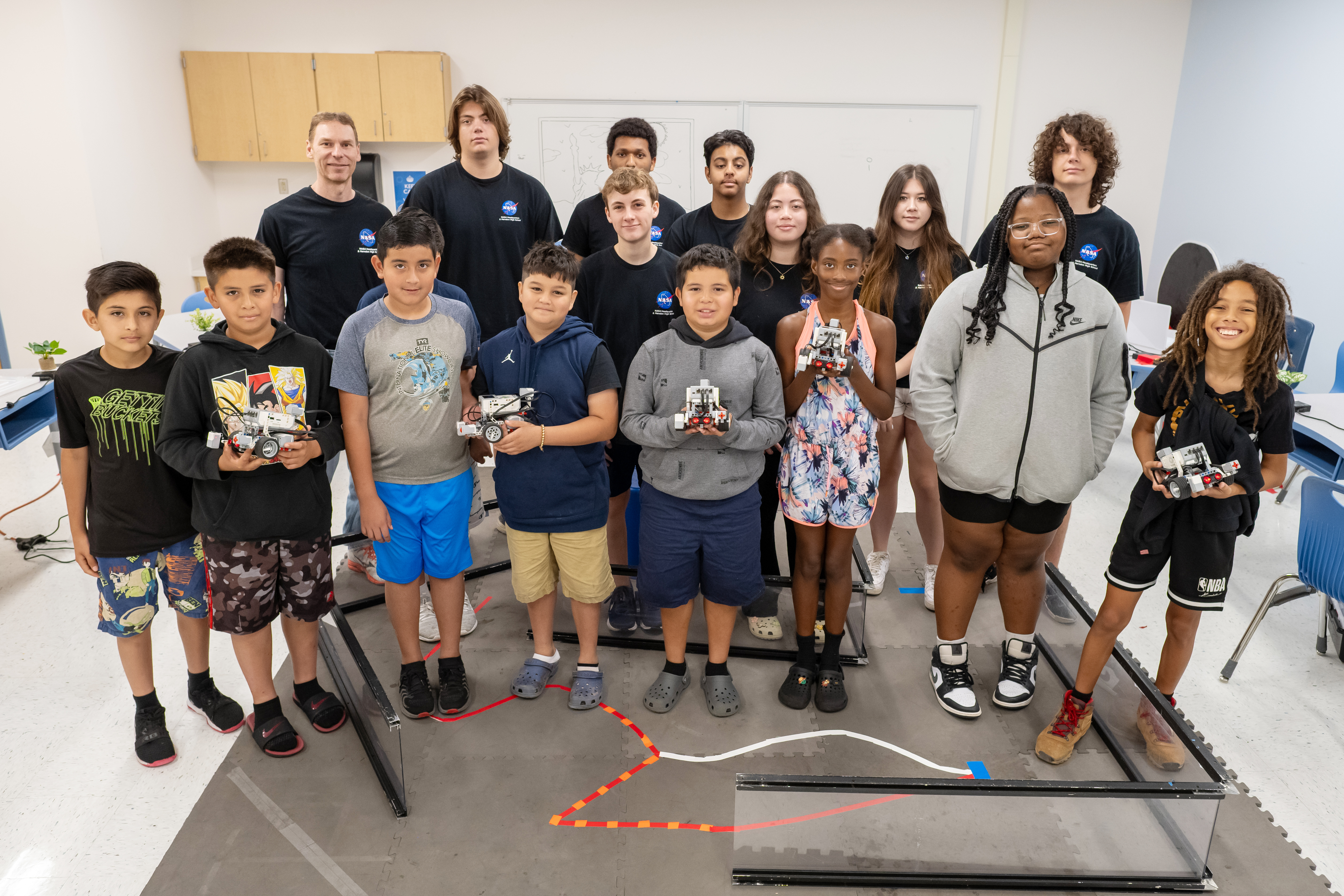 Students and instructors at Clearview Elementary School's robotics camp pose for a photo. Standing in a group, the eight Clearview students stand at front, smiling and holding their LEGO robots. Volunteer instructors, in matching black shirts bearing the NASA logo, stand in back. 