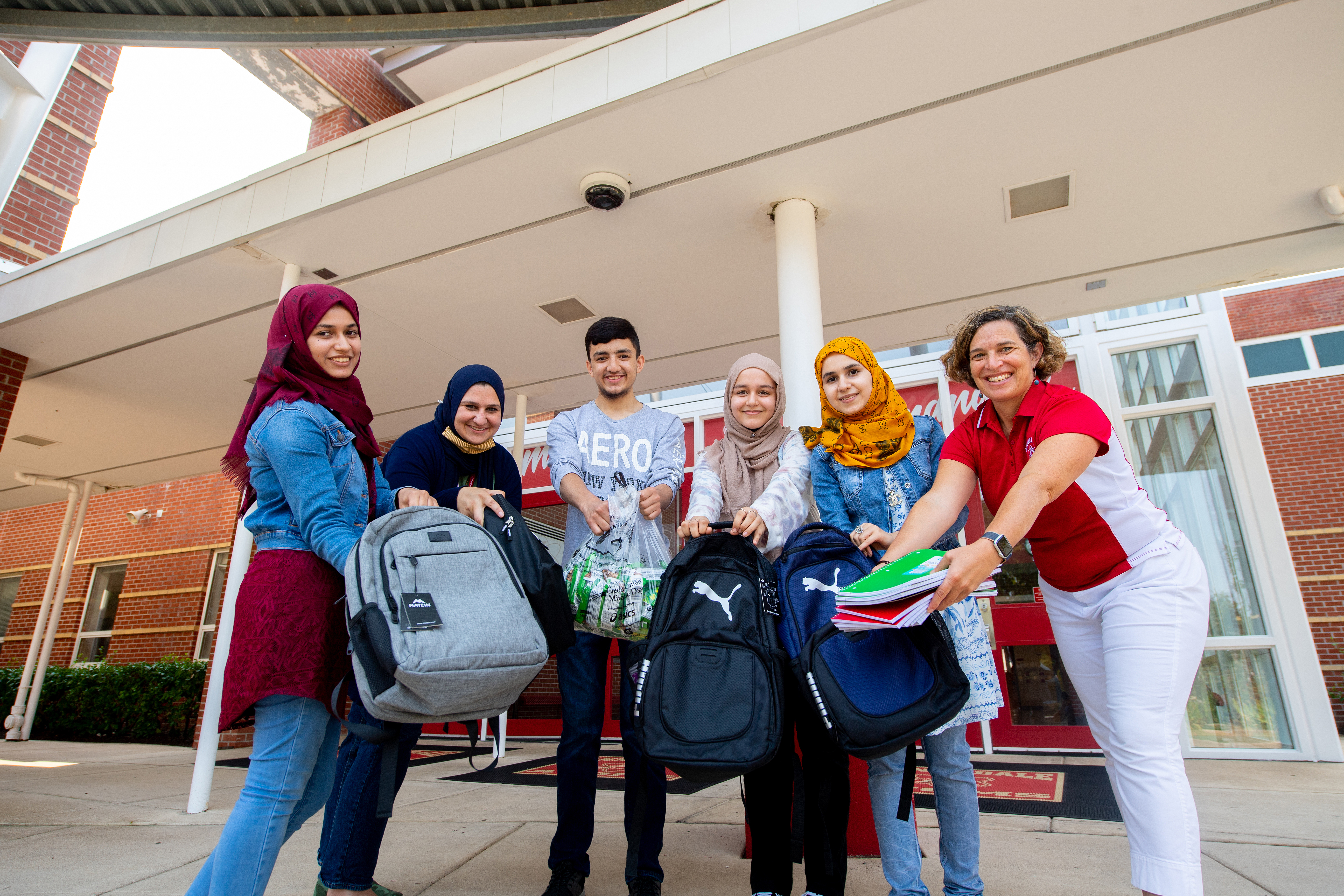 Sosan, Husna, Annandale High School assistant principal Sarah Eqab, Multilingual Education Department Chair Meredith Hedrick, and two other Dunya Club founders Husna's older  sister Khujasta Basiri and Ahsanullah Luddin, pose with supplies they collected for new refugee students in 2021. 