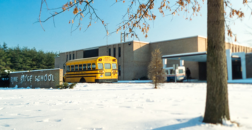 Photograph of the front exterior of Pine Ridge Elementary School in the wintertime. There is snow on the ground a school bus is parked in front of the building.