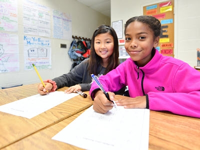 two students writing on paper at a desk