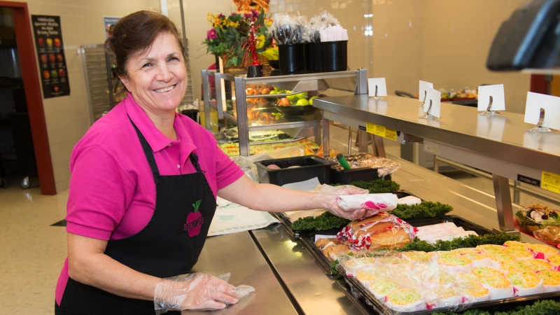 Food service worker holding a food item to hand to a student