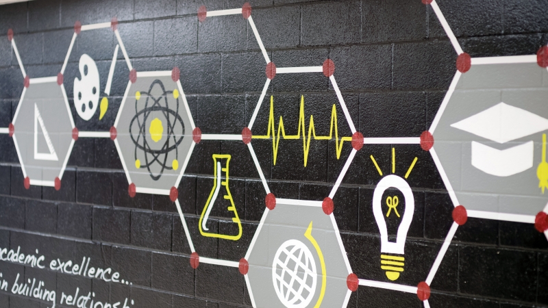 A wall mural of various education symbols, a graduation cap, a triangle, a beaker, a lightbulb, a globe.