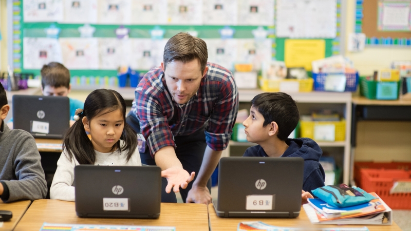 male teacher working with two young students who are working on laptops