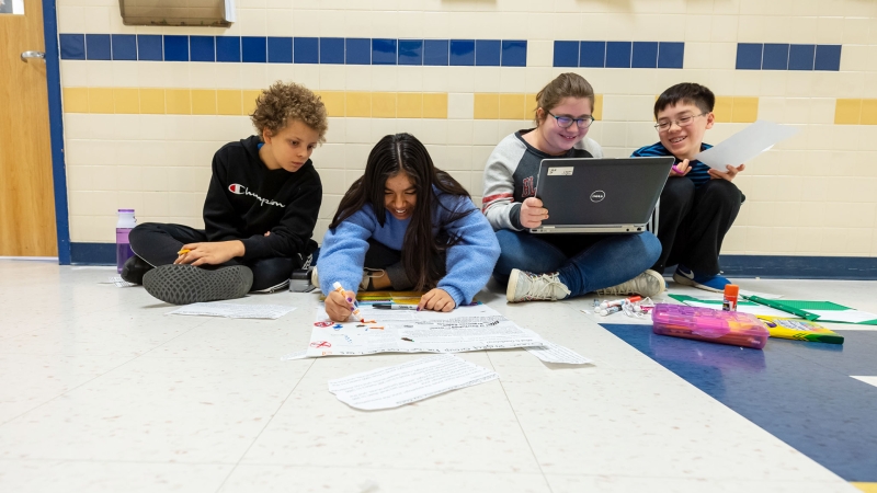 four students sitting outside a classroom collaborating