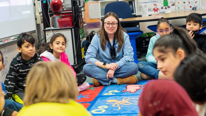 A counselor sits on the floor talking with students