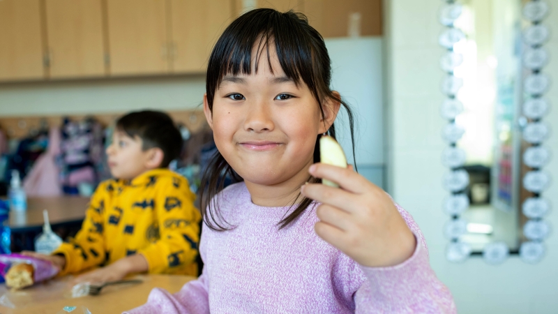 A young student holds an apple slice. 