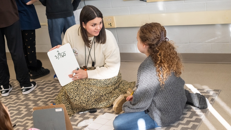 A teacher works with a student while sitting on the floor