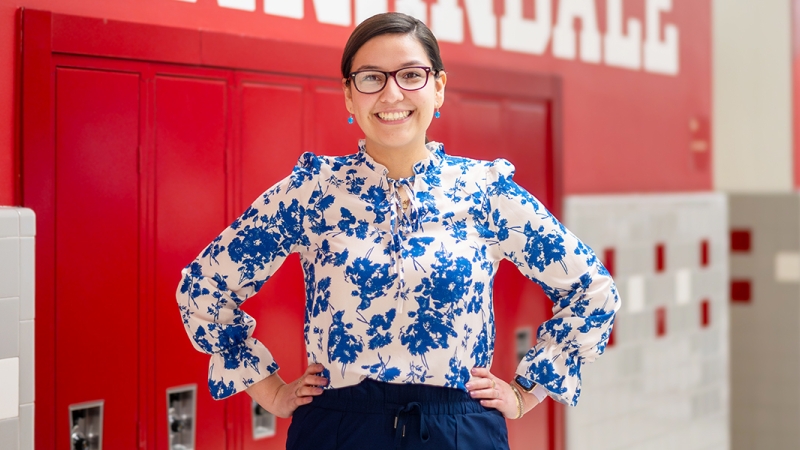 A young teacher stands in a high school hallway. 