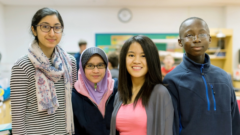 four students in a classroom looking at the camera