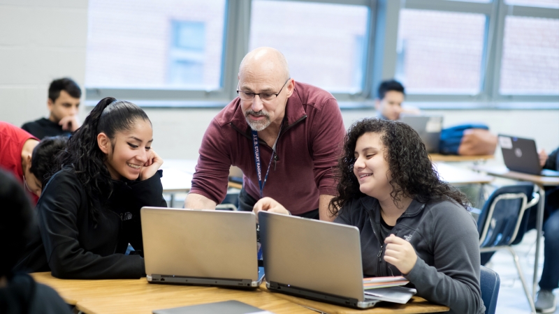 a male staff member interacting with two female students