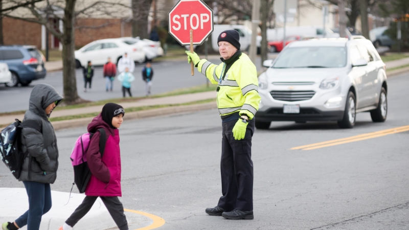 A crossing guard holds up a stop sign as two students cross the street