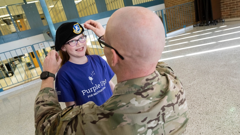 A man in military dress adjusts his hat on his daughter's head. 