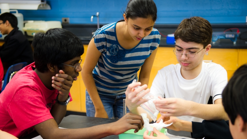 two female students working on a science project with a male student