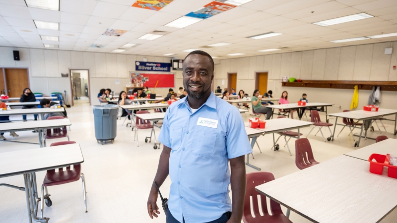 Frank Sarfo, a custodian, stands in a school cafeteria