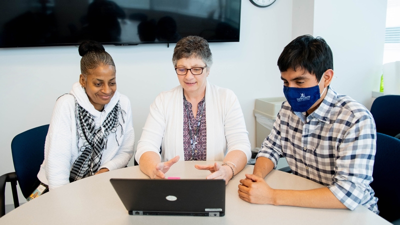 Three adults gather around an open laptop