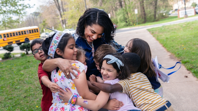 A teacher hugs young students