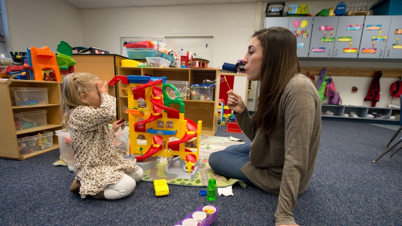 a teacher and girl sitting on the floor playing with toys