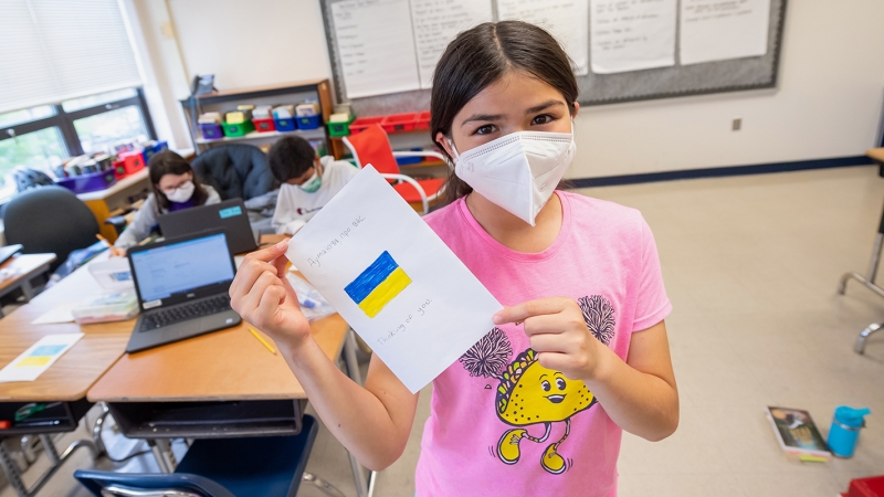 Student holds a card she wrote for a refugee child. 