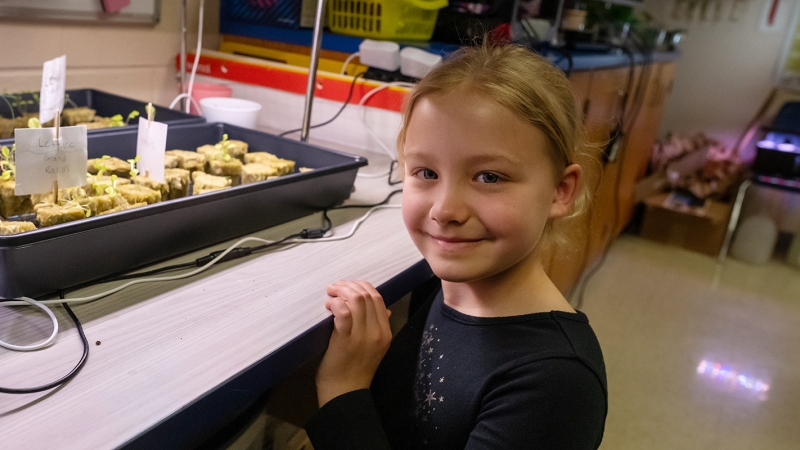 A smiling student posts next to a tray of growing sprouts. 