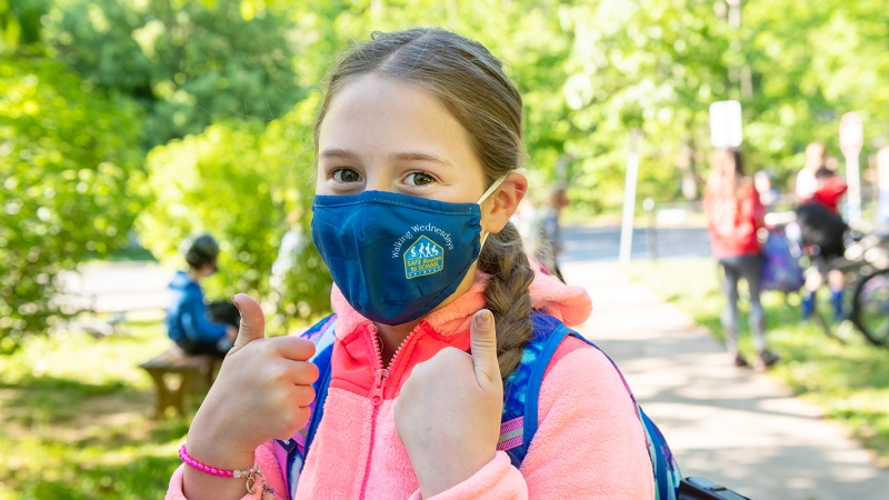 Girl in mask giving a thumbs up. 