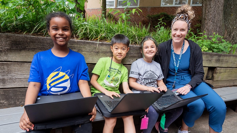 students and teacher on bench outside of school