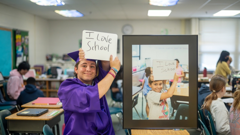 A student dressed in cap and gown holds up a sign that says "I love school" next to a photo of him as a fourth grader holding up a similar sign. 