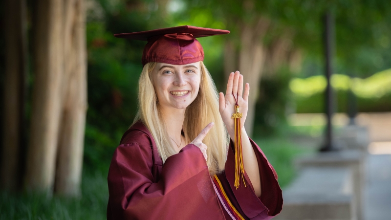 A graduate dressed in cap and gown points at her tassel