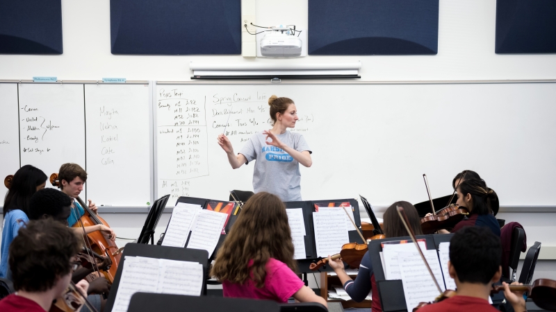 Orchestra teacher leads students playing stringed instruments