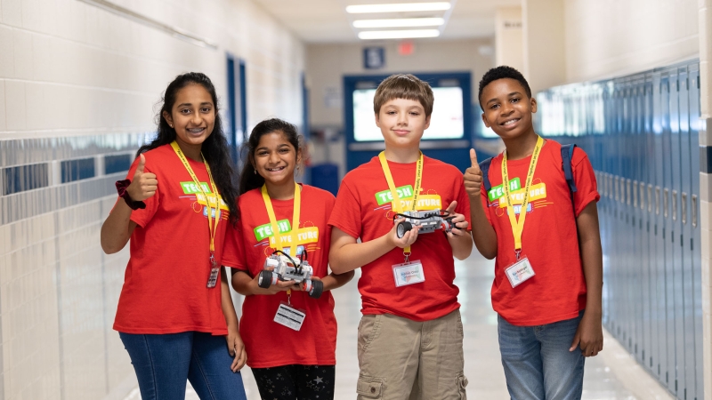 four students standing in a school hallway looking at the camera