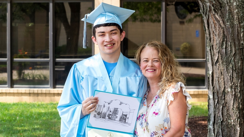 Logan in his graduate gown being hugged by his mother