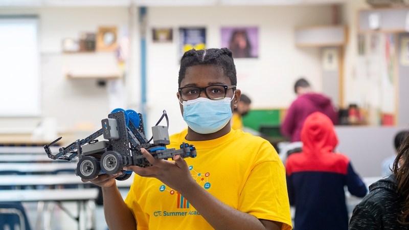 Student at summer camp holding up a robot.