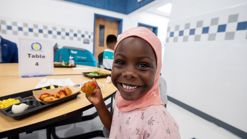 A girl eats corn dog nuggets in a school cafeteria