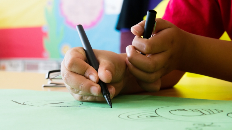 student holding a pen in one hand and the cap in the other while drawing on paper