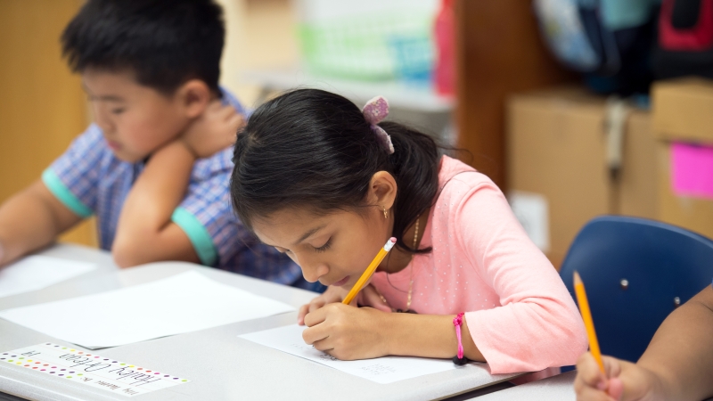 female student sitting at a desk beside other students taking a test