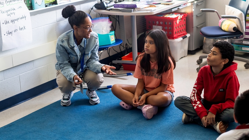 Jasmine Piernas talks to students while crouching on the floor