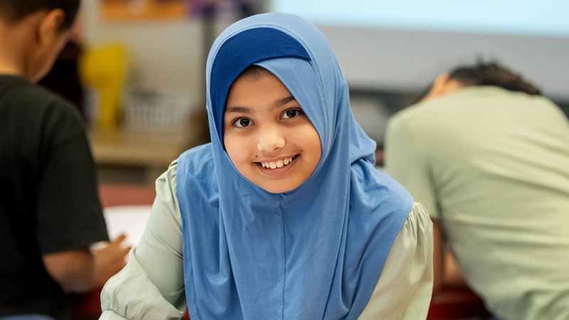 A young girl wearing a head scarf smiling