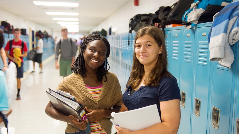 two female students standing in front of blue lockers in a school hallway