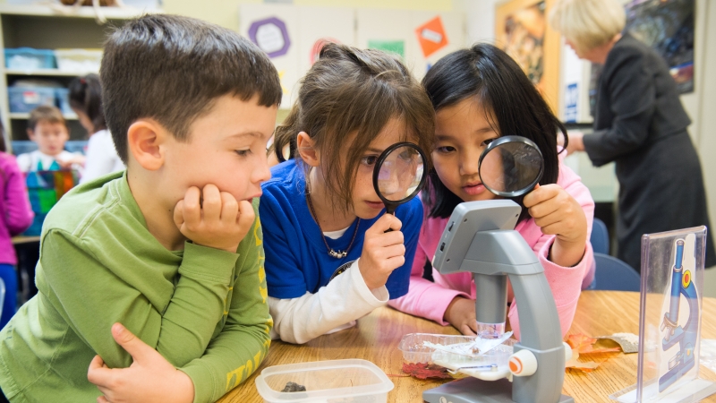 students looking through a magnifying lens doing a science experiment