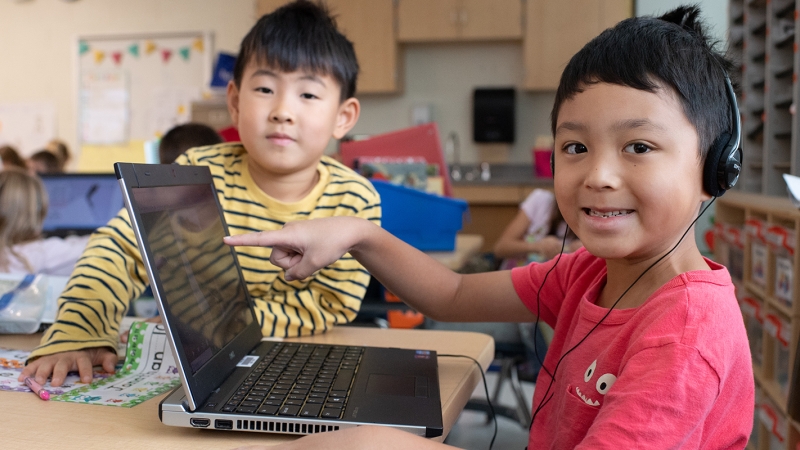 Two students sitting at a desk working on a laptop