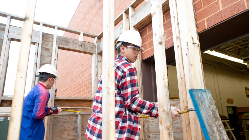 two students wearing hard hats framing out a wall