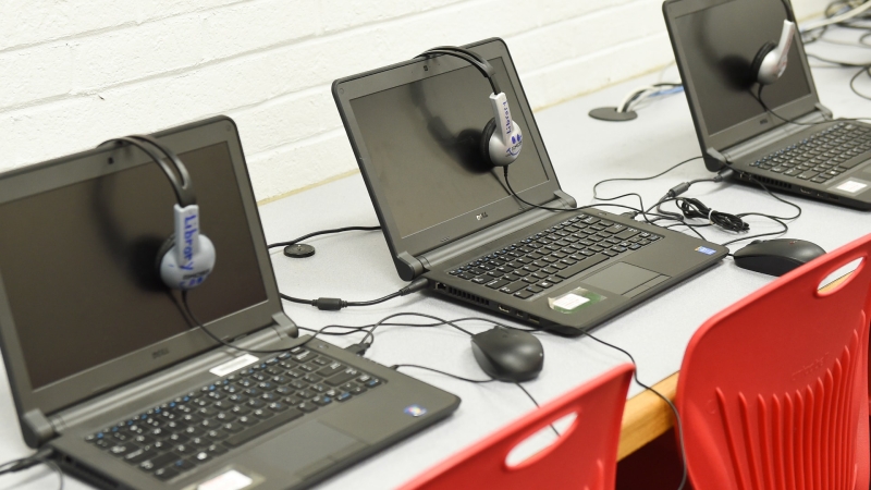three open laptops in a row with headphones hung over the lid