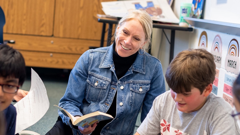 Smiling teacher with book working with students on classroom carpet