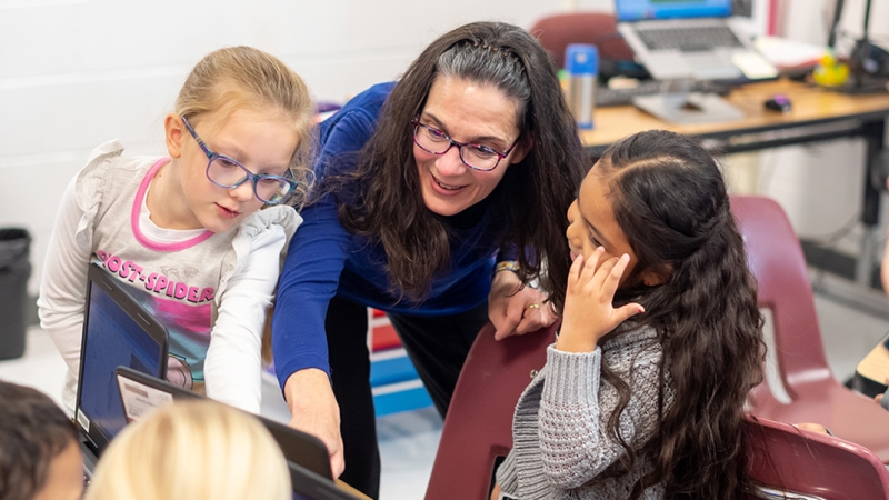 Teacher working with a group of students around a laptop computer.