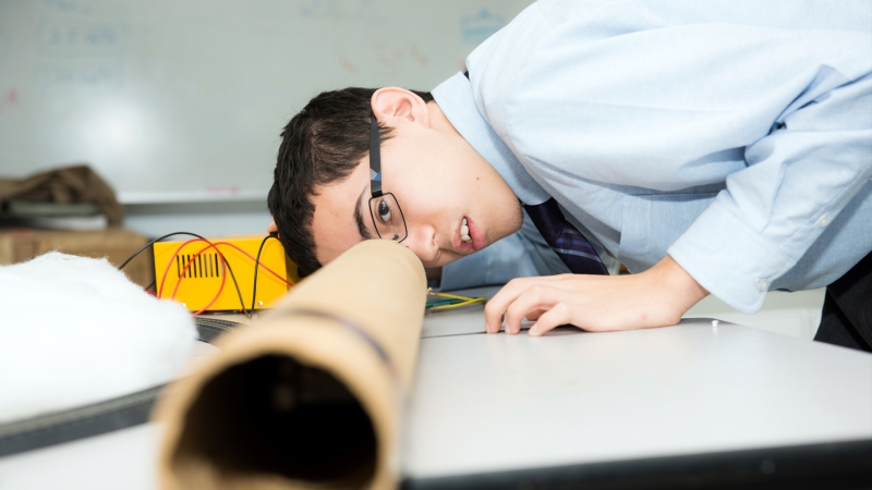 male student looking through a long cardboard tube