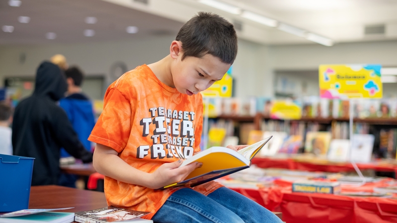 A young boy reads a book in a library 