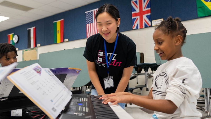 A student helps a younger student practice playing a keyboard