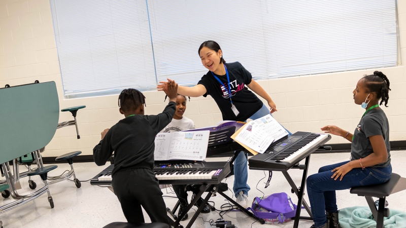 A student mentor high fives a student learning the piano